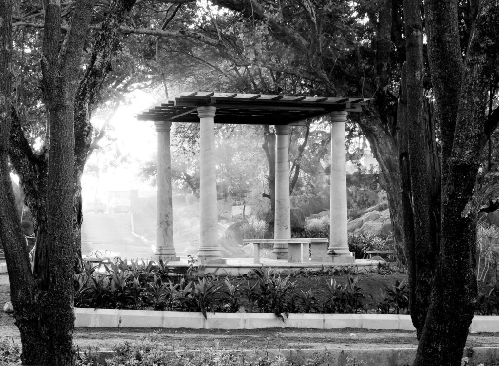 A serene monochrome image of a gazebo surrounded by lush trees in a tranquil park.